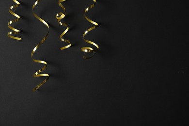 Shiny golden serpentine streamers on black background, flat lay. Space for text