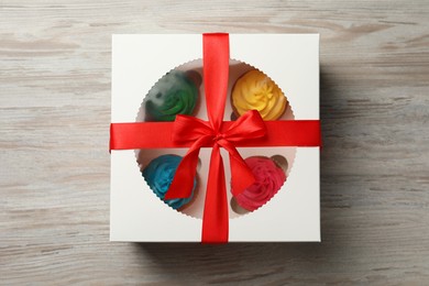 Box with delicious colorful cupcakes on white wooden table, top view