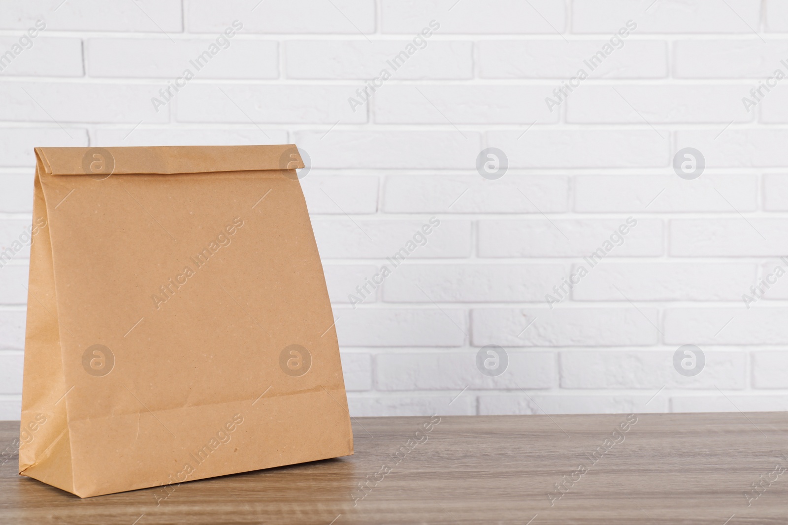 Photo of Paper bag on table against brick wall. Mockup for design