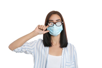 Photo of Young woman wiping foggy glasses caused by wearing disposable mask on white background. Protective measure during coronavirus pandemic
