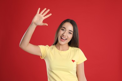 Woman in yellow t-shirt showing number five with her hand on red background