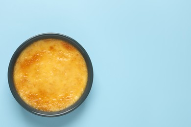 Delicious creme brulee in ceramic ramekin on light blue background, top view. Space for text