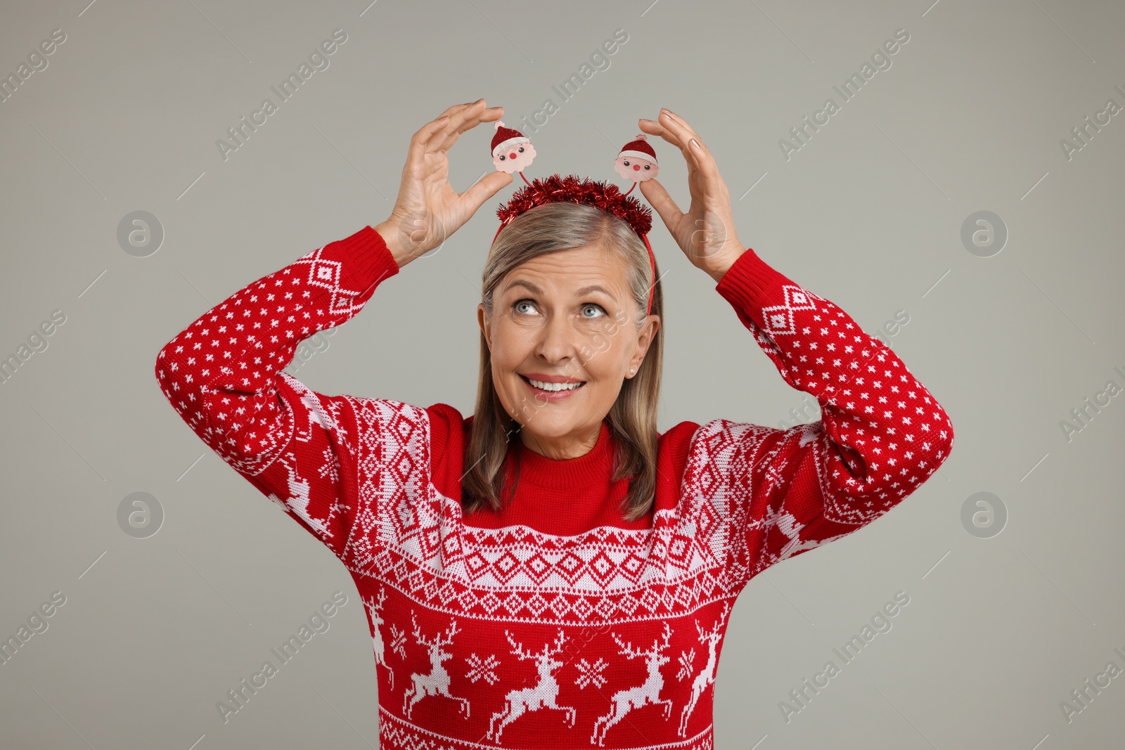 Photo of Happy senior woman in Christmas sweater and Santa headband on grey background