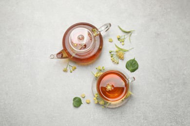 Tasty tea and linden blossom on light grey table, flat lay