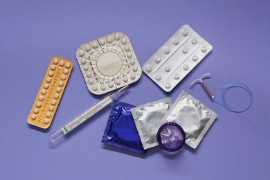 Photo of Contraceptive pills, condoms, intrauterine device and thermometer on violet background, flat lay. Different birth control methods