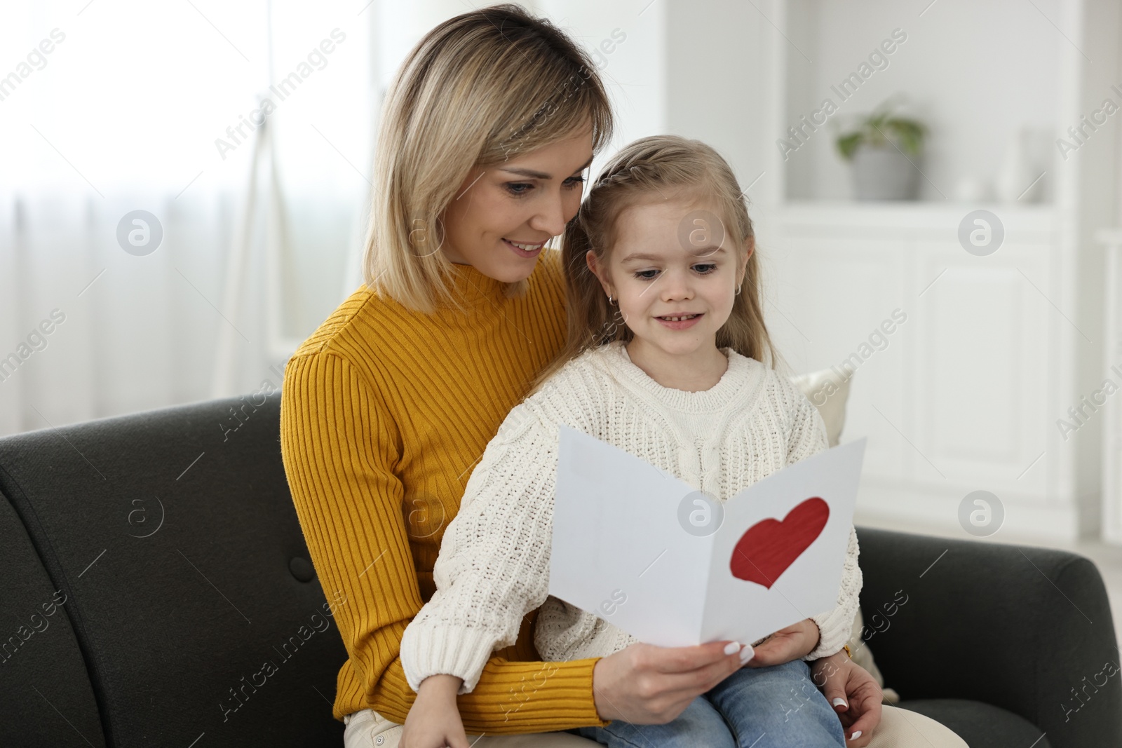 Photo of Little daughter congratulating her mom with greeting card at home. Happy Mother's Day