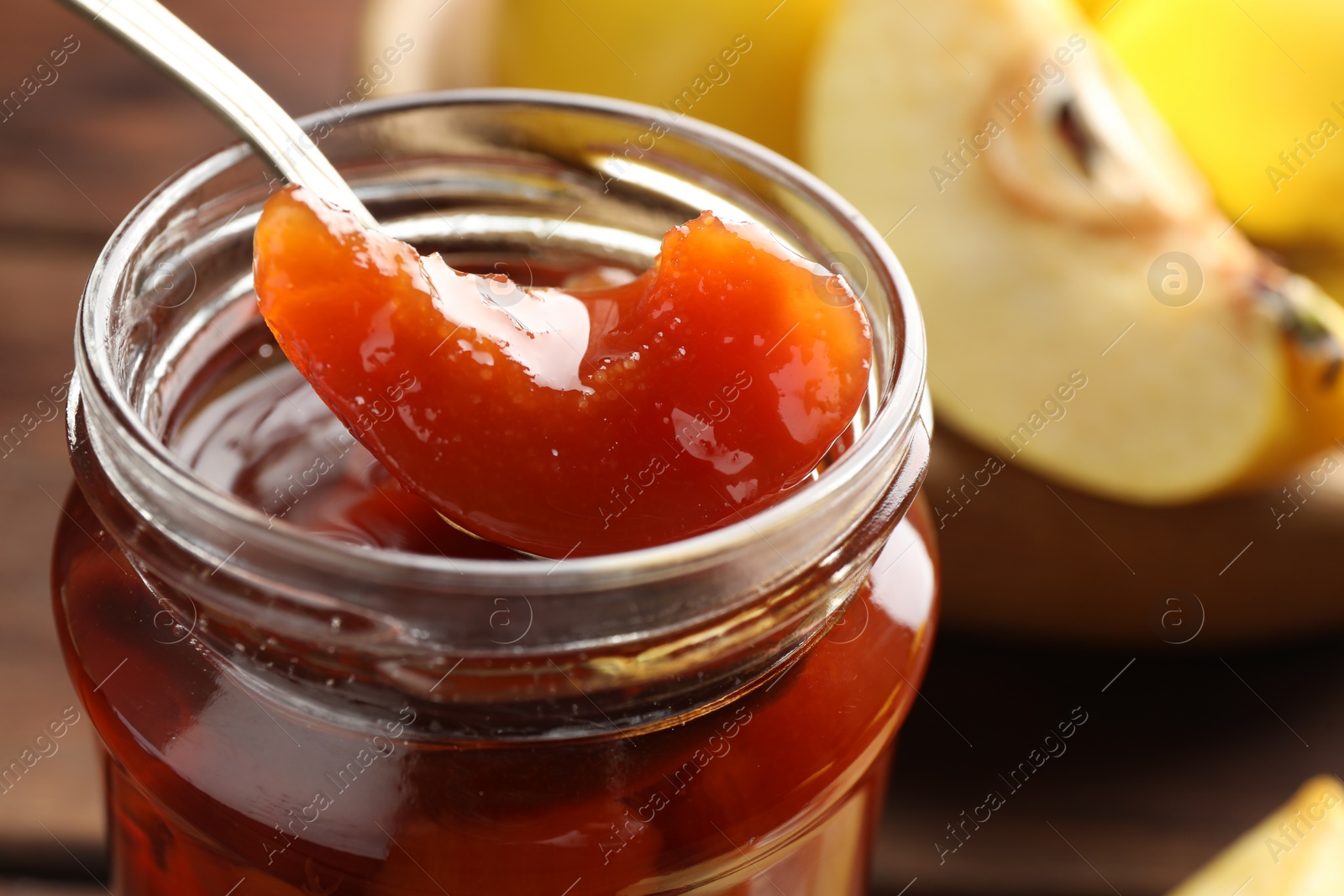 Photo of Taking tasty homemade quince jam from jar at table, closeup