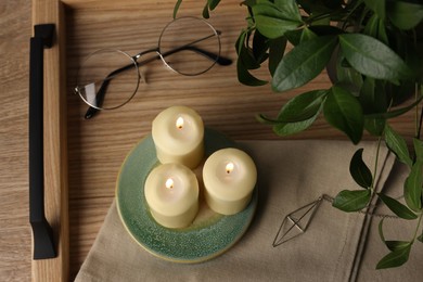 Eyeglasses, burning candles, bijouterie and houseplant on wooden table, above view