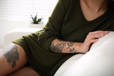 Photo of Beautiful woman with tattoos on body resting in living room, closeup