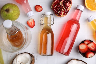 Tasty kombucha in glass bottles and fresh fruits on white tiled table, flat lay