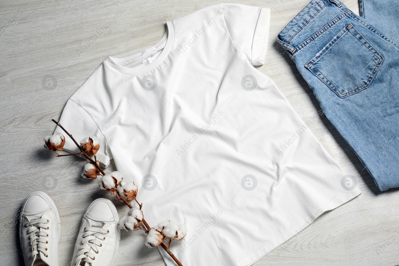 Photo of Stylish t-shirt, sneakers and jeans on white wooden background, flat lay