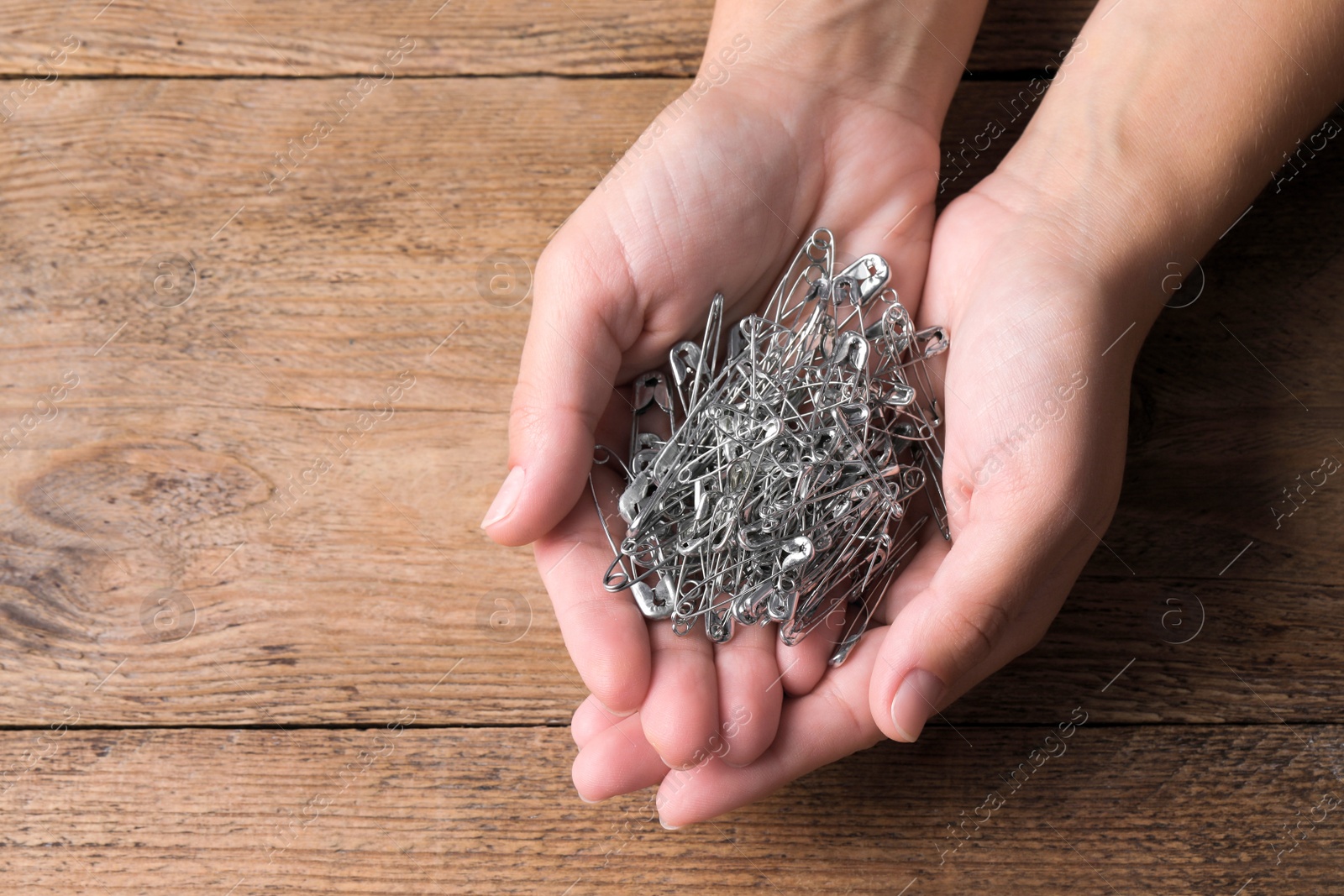 Photo of Woman holding pile of safety pins at wooden table, top view. Space for text