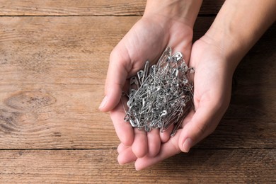 Photo of Woman holding pile of safety pins at wooden table, top view. Space for text