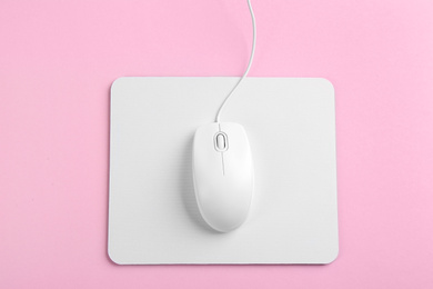 Photo of Modern wired mouse and white pad on pink background, top view
