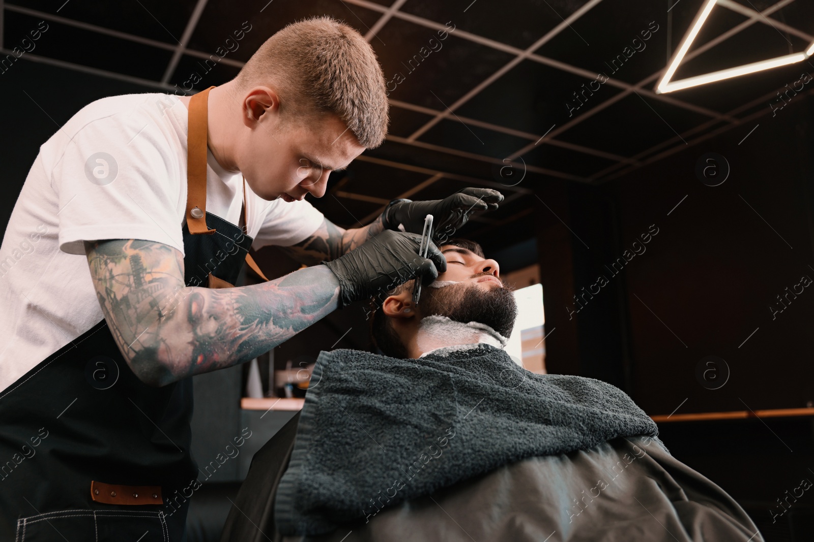 Photo of Professional hairdresser working with bearded client in barbershop