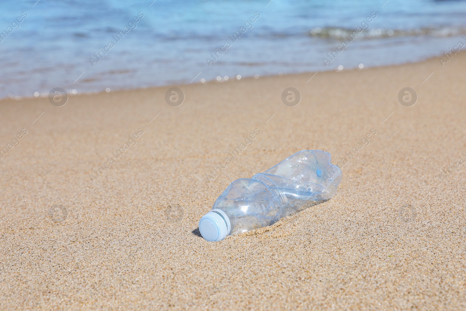 Photo of Used plastic bottle on sand near water. Recycling problem