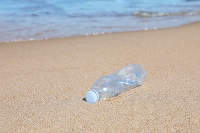 Used plastic bottle on sand near water. Recycling problem