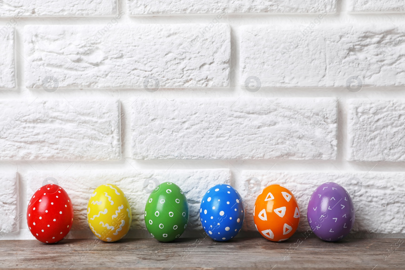 Photo of Decorated Easter eggs on table near brick wall. Space for text