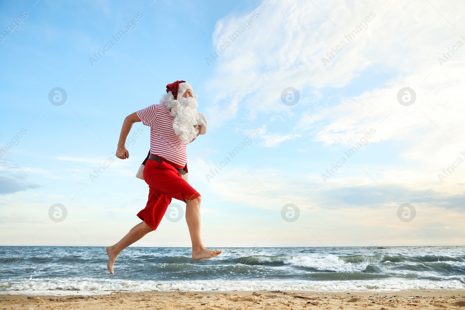 Photo of Santa Claus having fun on beach, space for text. Christmas vacation