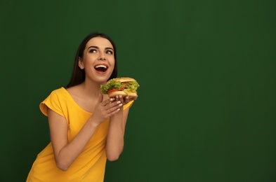 Young woman eating tasty burger on color background. Space for text