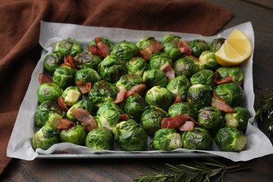 Photo of Delicious roasted Brussels sprouts, bacon, lemon and rosemary on wooden table