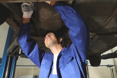 Photo of Professional mechanic fixing lifted car at automobile repair shop