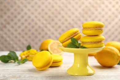 Photo of Delicious macarons, mint and lemons on white wooden table. Space for text