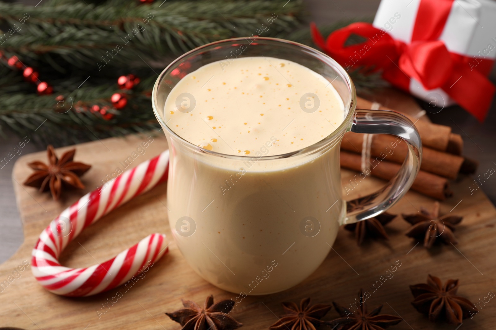 Photo of Glass of delicious eggnog, candy cane and anise stars on wooden table, closeup