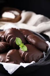 Delicious chocolate covered marshmallows with mint on black table, closeup