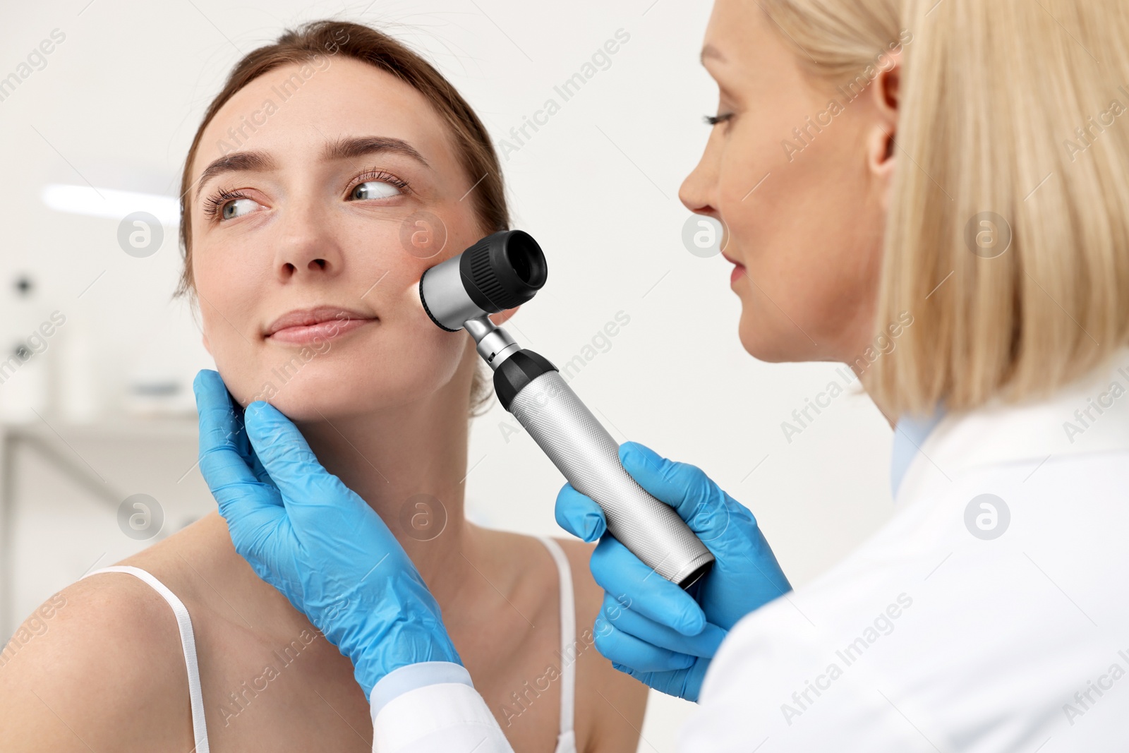 Photo of Dermatologist with dermatoscope examining patient`s face in clinic