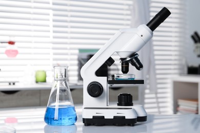 Photo of Laboratory analysis. Flask with blue liquid and microscope on white table indoors