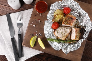 Photo of Pieces of delicious meat baked in foil with tomatoes and sauce on wooden table, flat lay