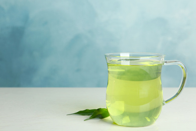 Photo of Cup of aromatic green tea and leaves on light wooden table. Space for text