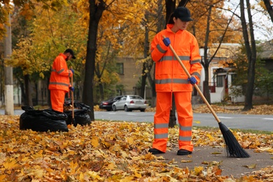 Street cleaners sweeping fallen leaves outdoors on autumn day