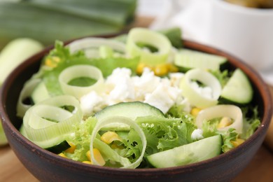 Bowl of tasty salad with leek and cheese on table, closeup