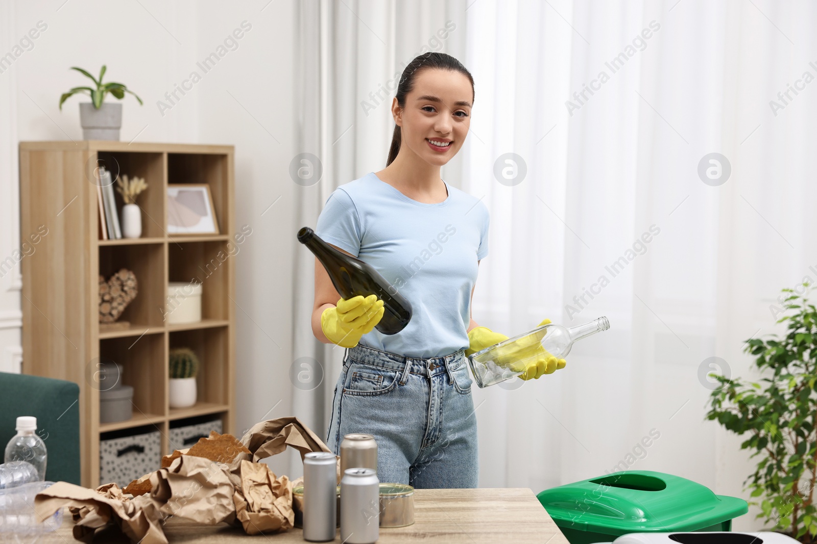 Photo of Garbage sorting. Smiling woman with glass bottles in room