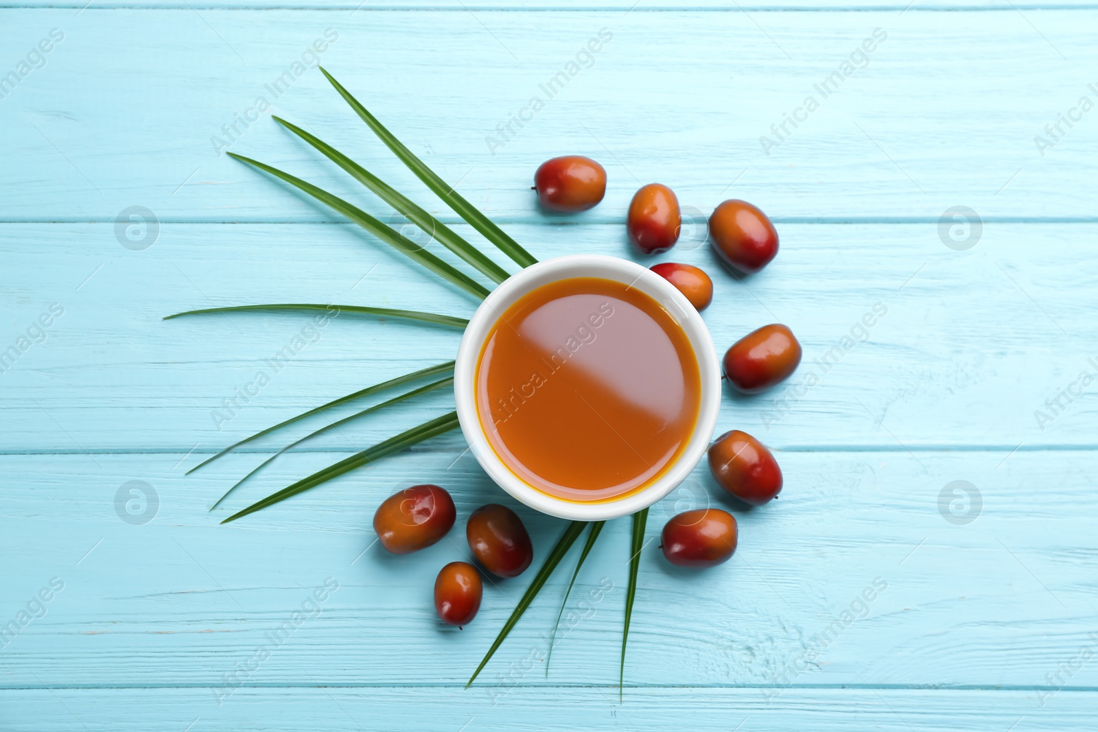 Photo of Palm oil in glass bowl, tropical leaf and fruits on light blue wooden table, flat lay