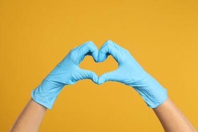 Photo of Doctor in medical gloves showing heart with hands on yellow background, closeup