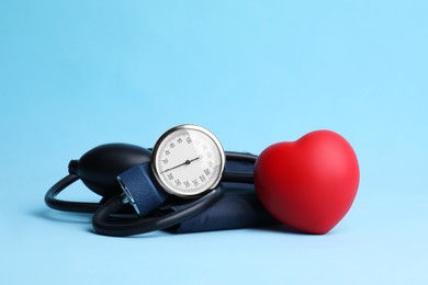 Photo of Blood pressure meter and toy heart on light blue background