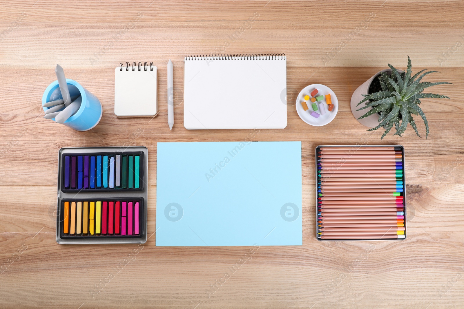 Photo of Layout with blank papers, soft pastels and other drawing supplies on wooden table at artist's workplace, top view. Space for design