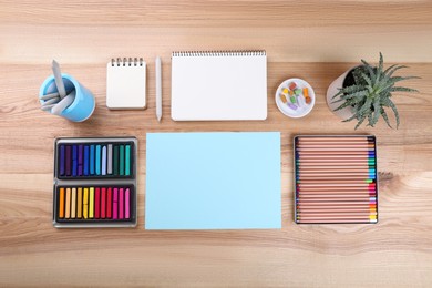 Layout with blank papers, soft pastels and other drawing supplies on wooden table at artist's workplace, top view. Space for design