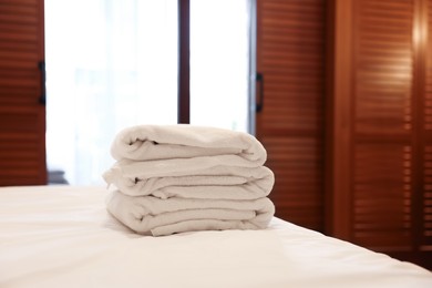 Stacked towels on bed in hotel room, space for text