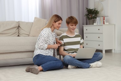 Happy mother and her teenage son spending time together with laptop on floor at home