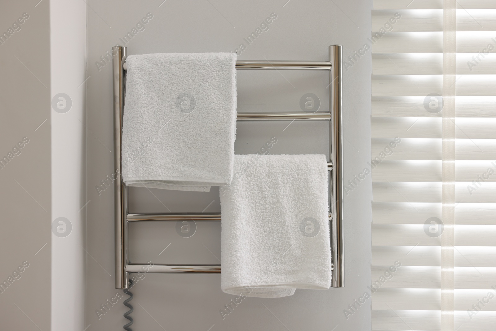 Photo of Heated rail with towels on white wall in bathroom