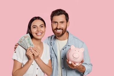 Photo of Happy couple with money and ceramic piggy bank on pale pink background