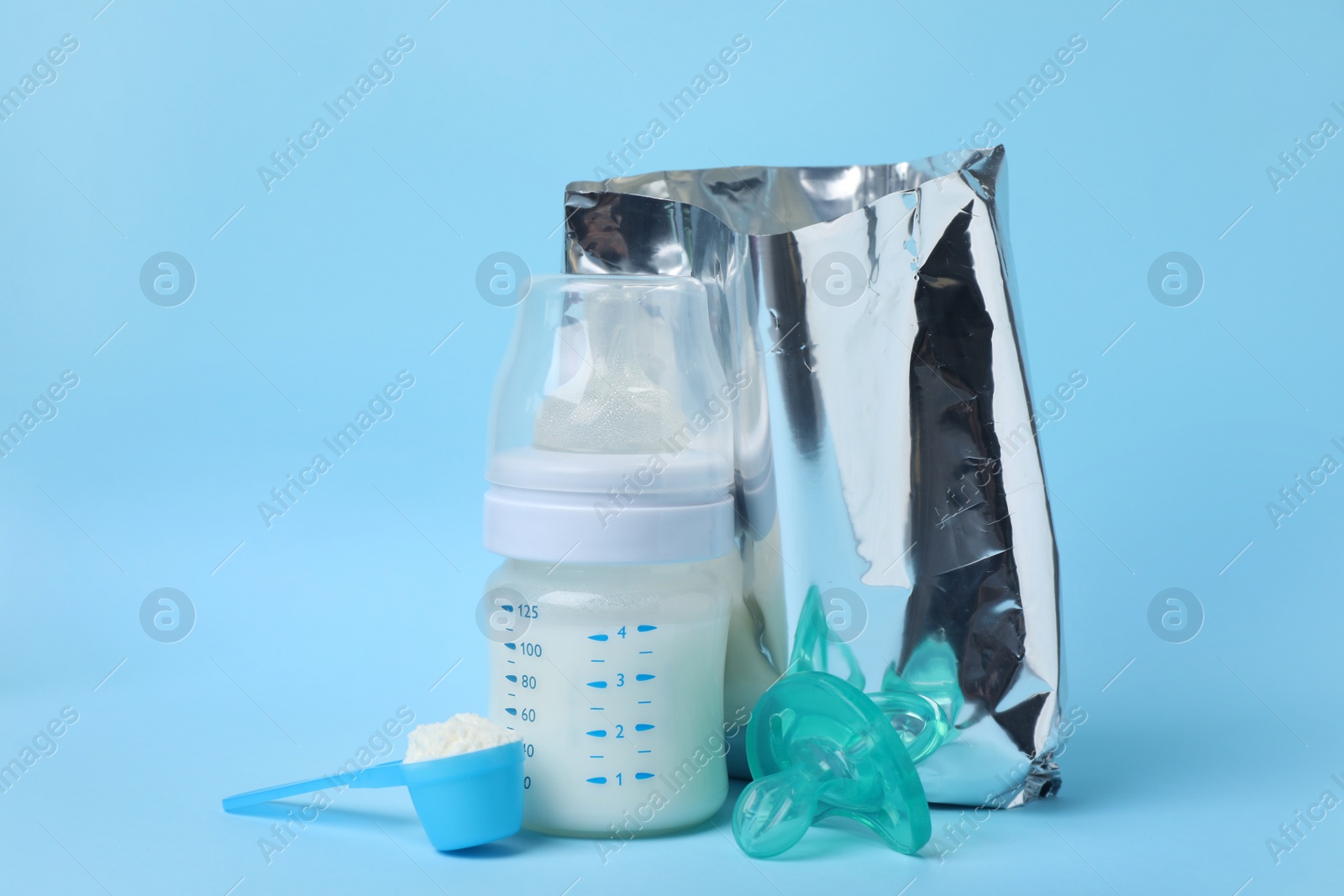 Photo of Bag of powdered infant formula, feeding bottle, scoop and pacifier on light blue background. Baby milk