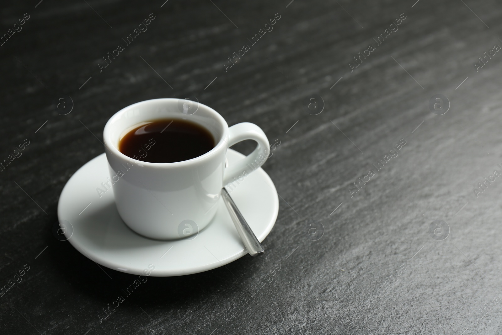 Photo of Hot coffee in cup and saucer on dark textured table, closeup. Space for text