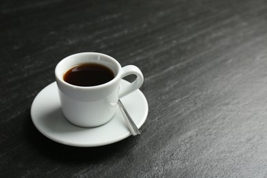 Hot coffee in cup and saucer on dark textured table, closeup. Space for text