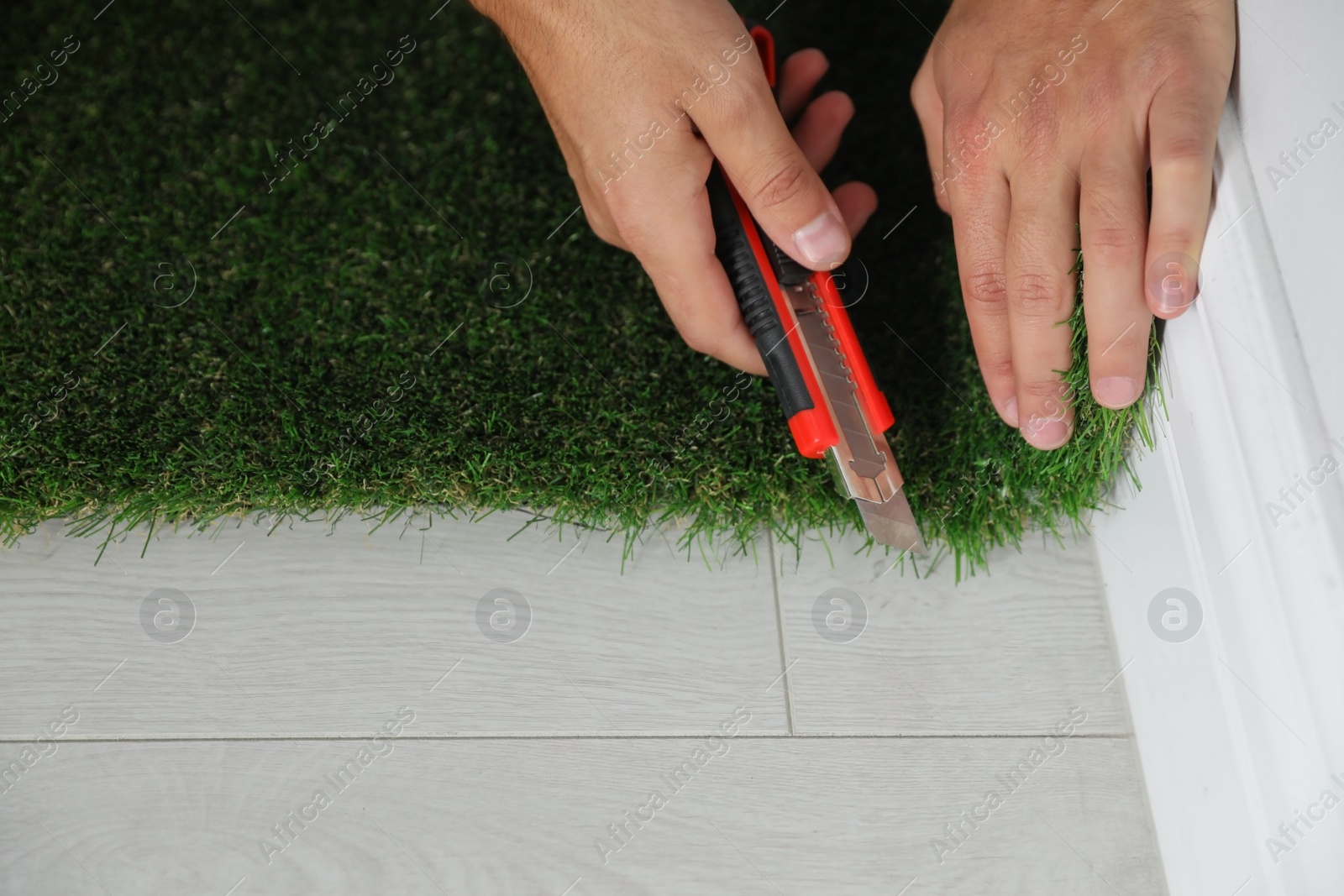 Photo of Man cutting artificial grass carpet indoors, closeup. Space for text