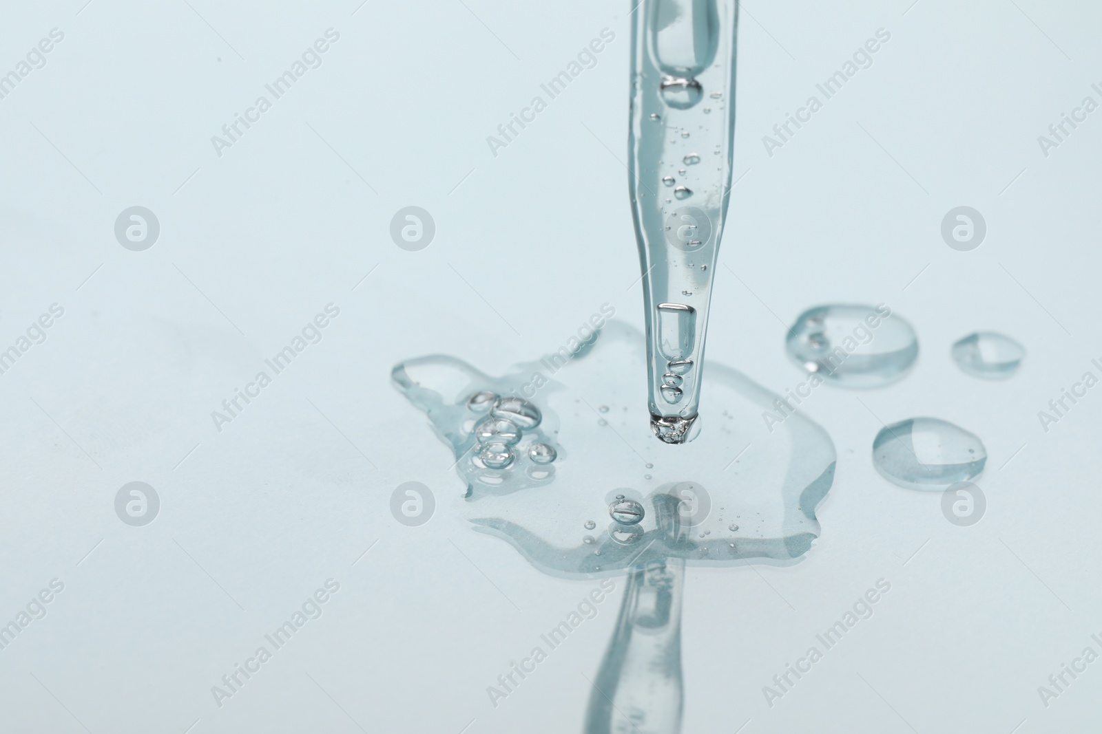 Photo of Glass pipette and transparent liquid on light background, closeup. Space for text